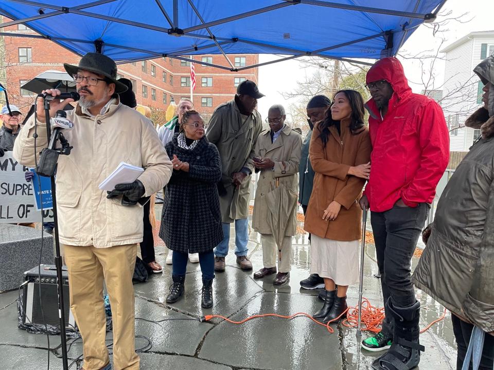 Will Arvelo speaks in support of Mamadou Dembele, right in red with Portsmouth Assistant Mayor Joanna Kelley at his side, during a protest held at the African Burying Ground Memorial Park in Portsmouth Sunday, Dec. 3, 2023.